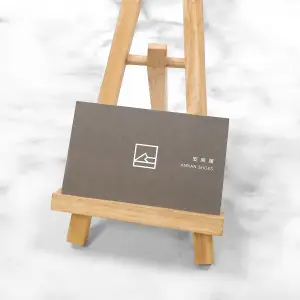 深咖啡色背景搭配白色線條logo，印於萊妮紙上。紙張布紋細密、質地厚實，使低調設計更具觸感層次與專業感。