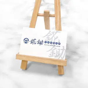 白底藍字圖文設計，萊妮紙的十字紋路讓名片整體在光線下稍帶一些陰影層次。左側品牌字體結合和風圖樣，呈現日本料理品牌的典雅風格。
